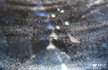Неравномерное распределение пузырьков воздуха и шихты в соответствии с ростовой зональностью в синтетическом сапфире. Метод синтеза - метод Вернеля. Режим просмотра - тёмнопольное освещение.