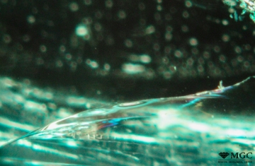 "Flash" effect (blue and yellow) from a crack in an emerald filled with organic matter (oil). View mode - transmitted light.