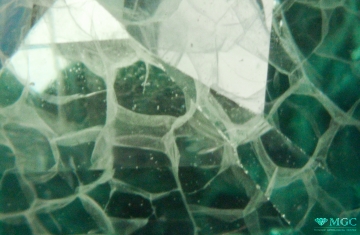 Flux "healing" of "forced" cracks in synthetic green corundum, imitating emerald. View mode - dark lighting.