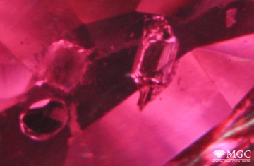 Включения циркона, кальцита (частично разрушен) и неопределённого минерала в термообработанном рубине. Режим просмотра - темнопольное освещение.